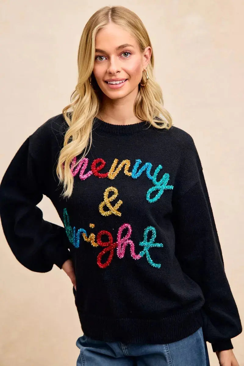 Front view of BiBi tinsel lettering holiday sweater with female model - hands on hip.