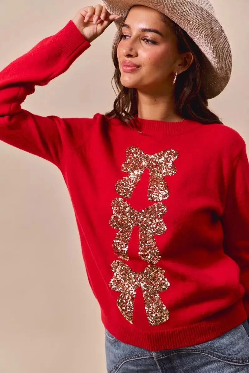 Red Christmas sweater with sequin bow ribbon detail on model posing with hat.