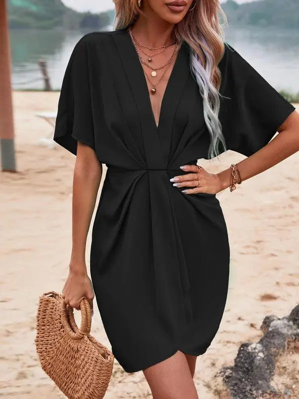 Batwing sleeve ruched dress front view in the color Black on female model posing with hand on hip.