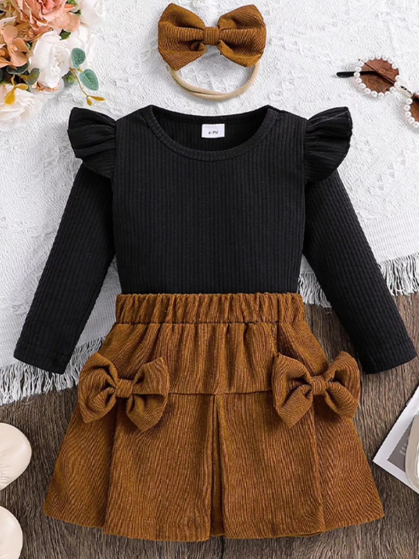 Front view of children’s ribbed top and bow skirt set with matching headband in brown and black.