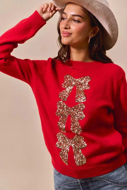 Red Christmas sweater with sequin bow ribbon detail on model posing with hat.