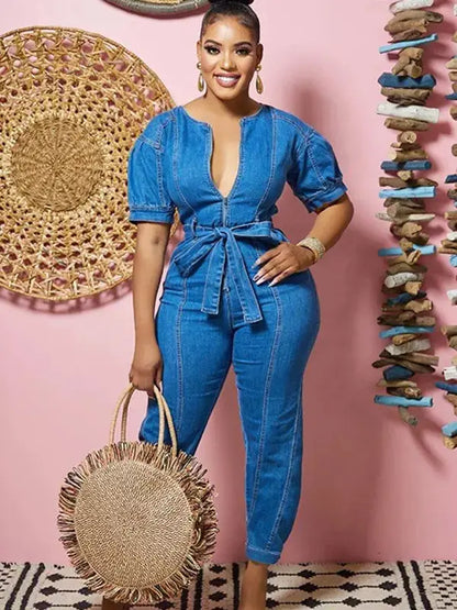 Woman in a blue denim outfit holding a straw bag against a pink wall with decorative elements.