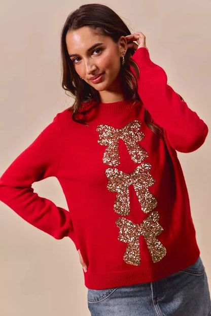 Red Christmas sweater with sequin bow ribbon detail on model posing with hand in hair.