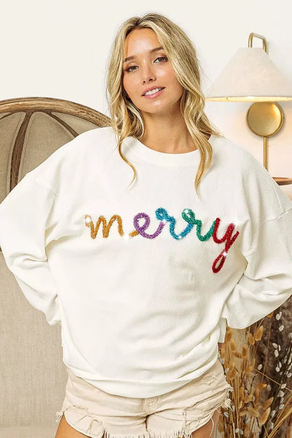 Model posing in festive Merry tinsel top with hands behind back.
