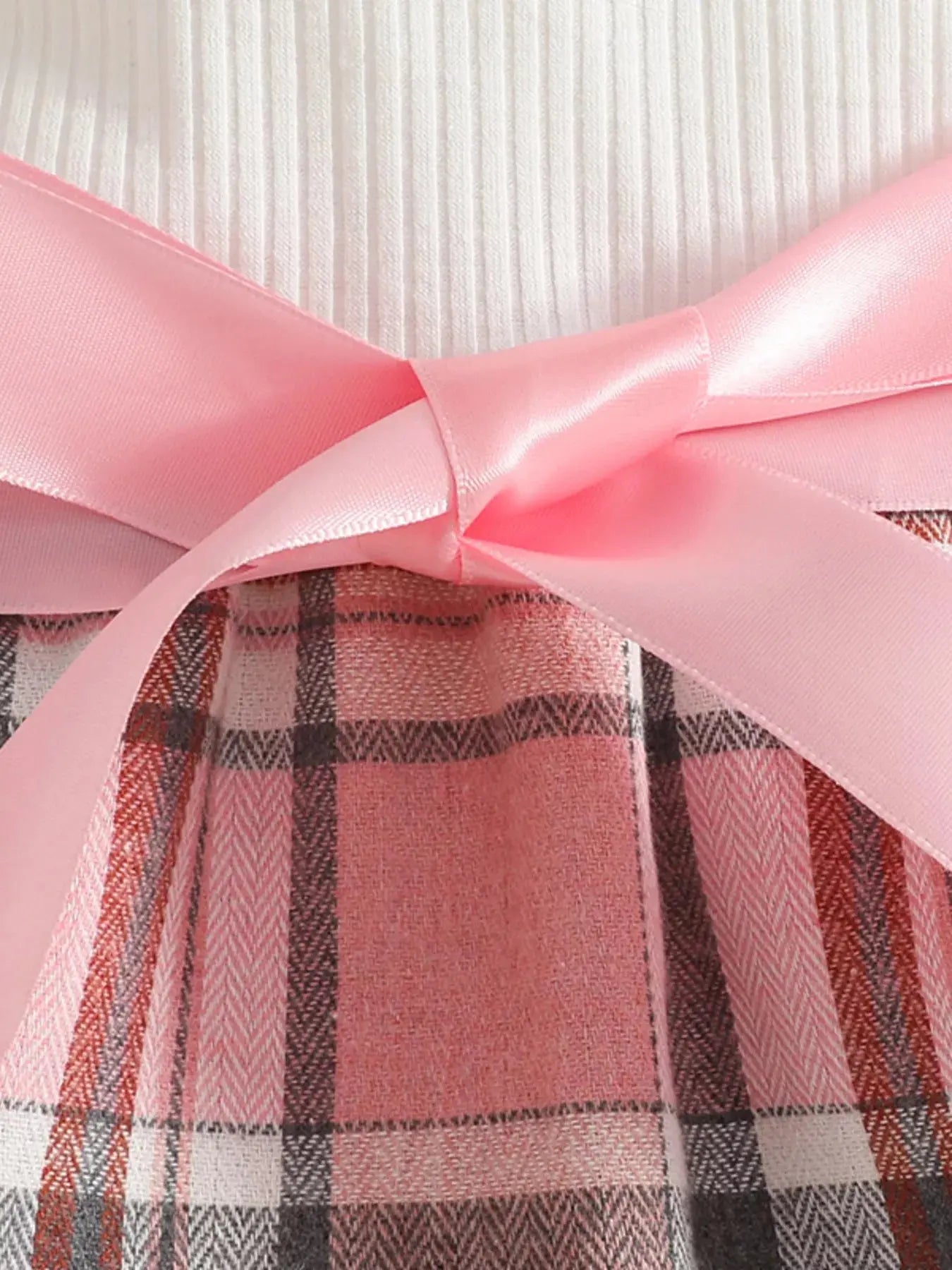 Flat lay of toddler girl plaid skirt outfit with details of front pink bow.